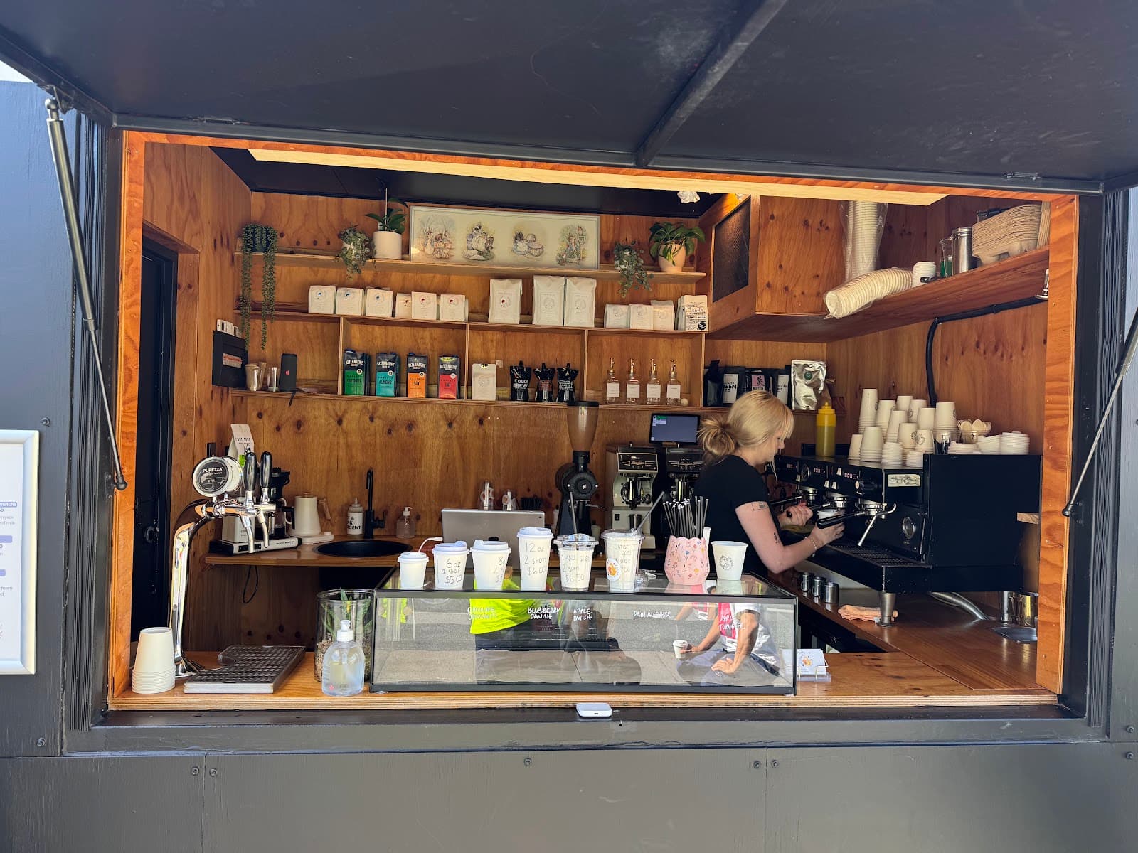 Inside the ames coffee hatch, with plywood-lined shelving, an espresso machine and a barista pulling a shot