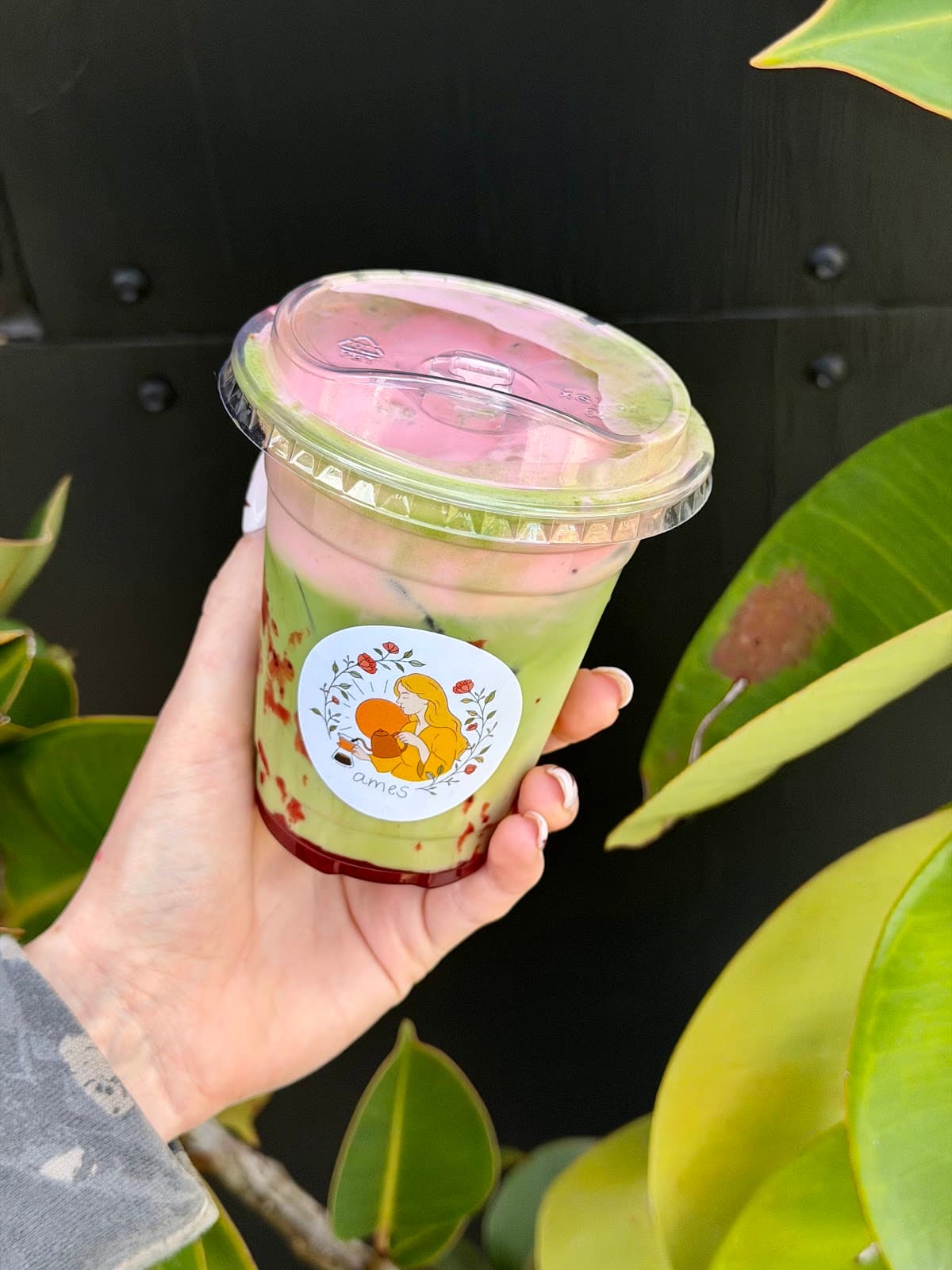 Iced matcha drink with strawberry cold foam, held up in front of the ames coffee window