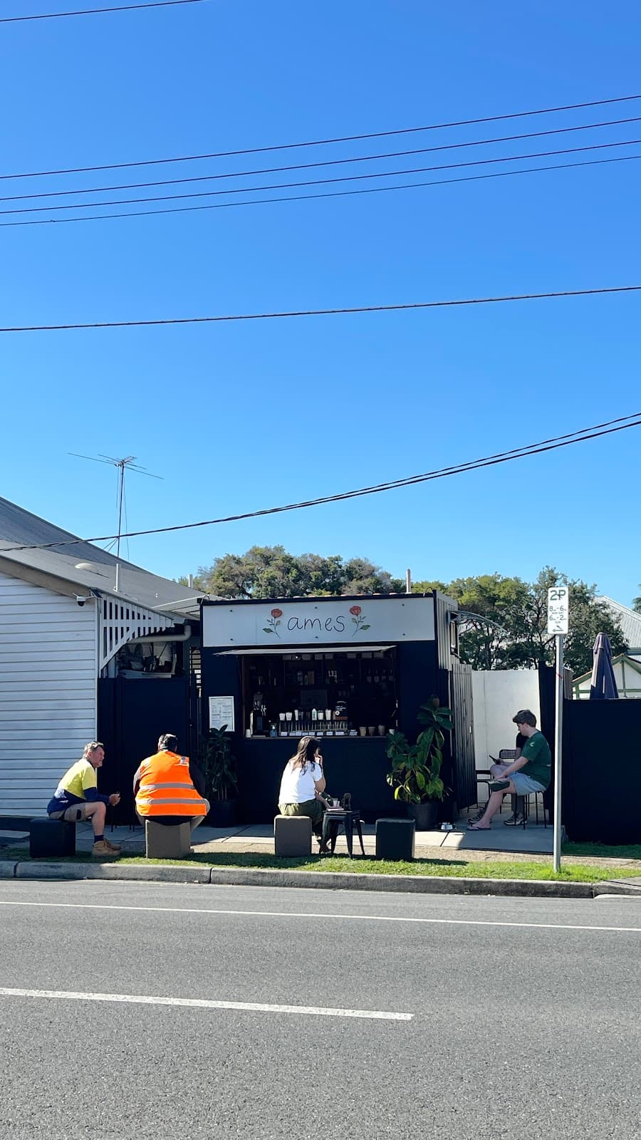 ames coffee viewed from across McLennan Street, with customers on stools out front and the Queenslander house next door